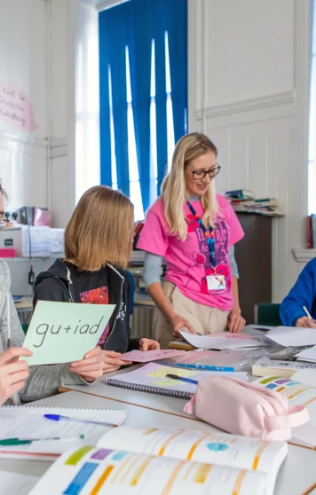 Gaelic lecturer supporting students in a language learning activity, with students holding vocabulary cards and engaging in conversation. Gaelic lecturer supporting students in a language learning activity, with students holding vocabulary cards and engaging in conversation.